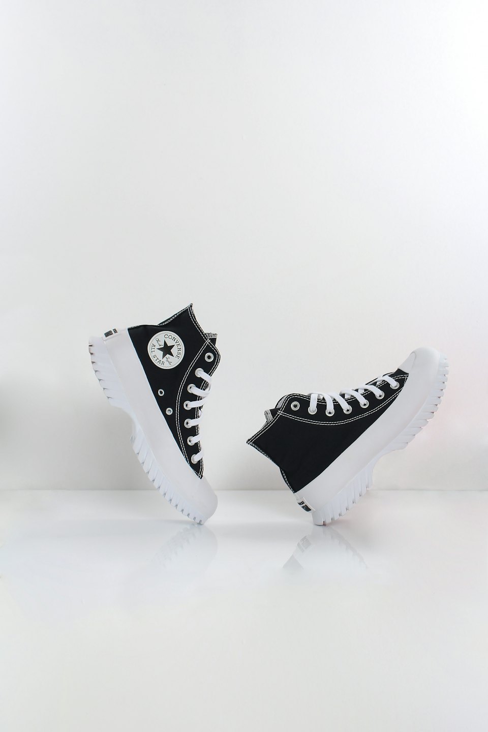 Schwarze und weiße High-Top-Sneaker auf einer weißen reflektierenden Oberfläche.