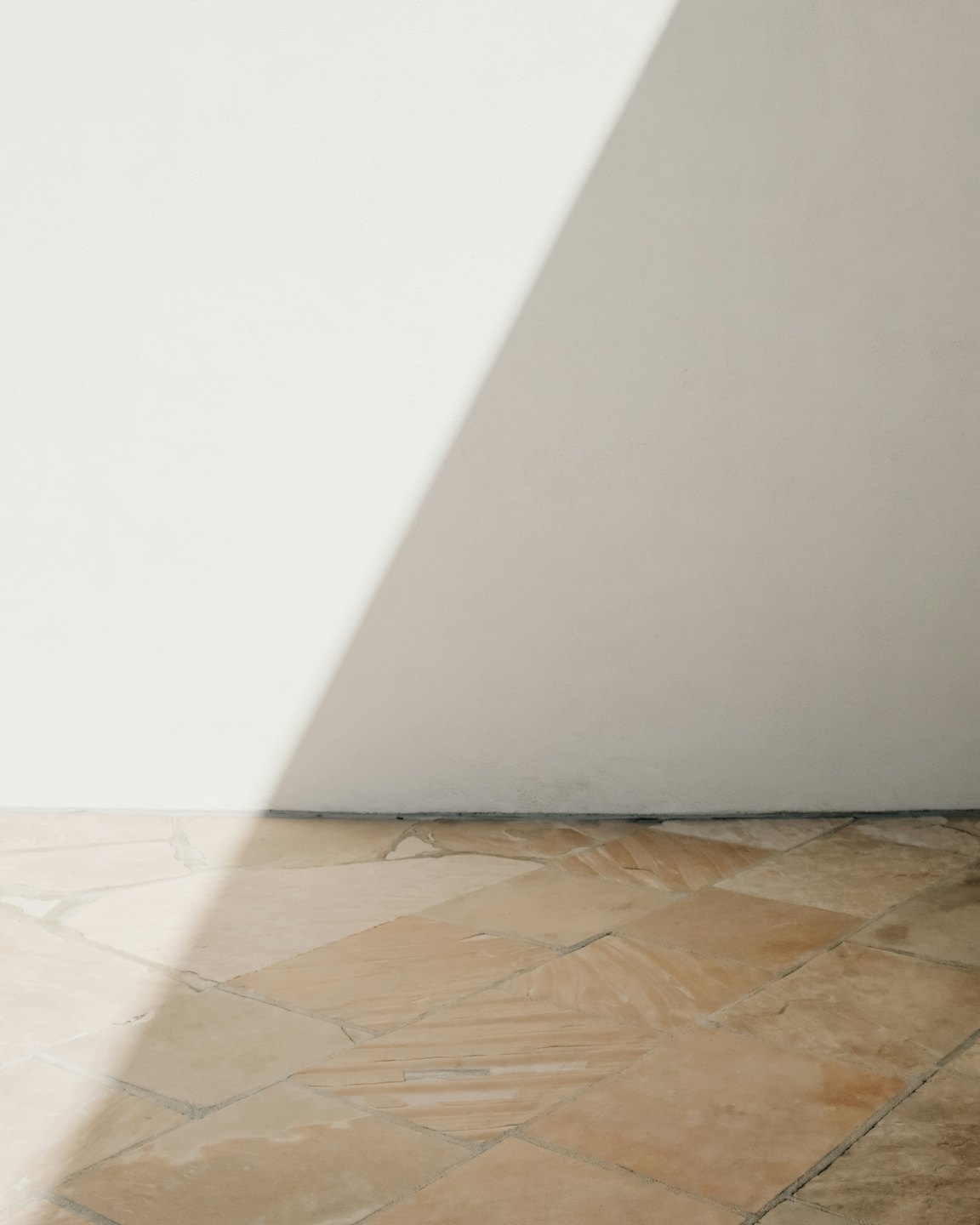 Sonnenlicht wirft einen diagonalen Schatten über einen Steinboden und eine weiße Wand.