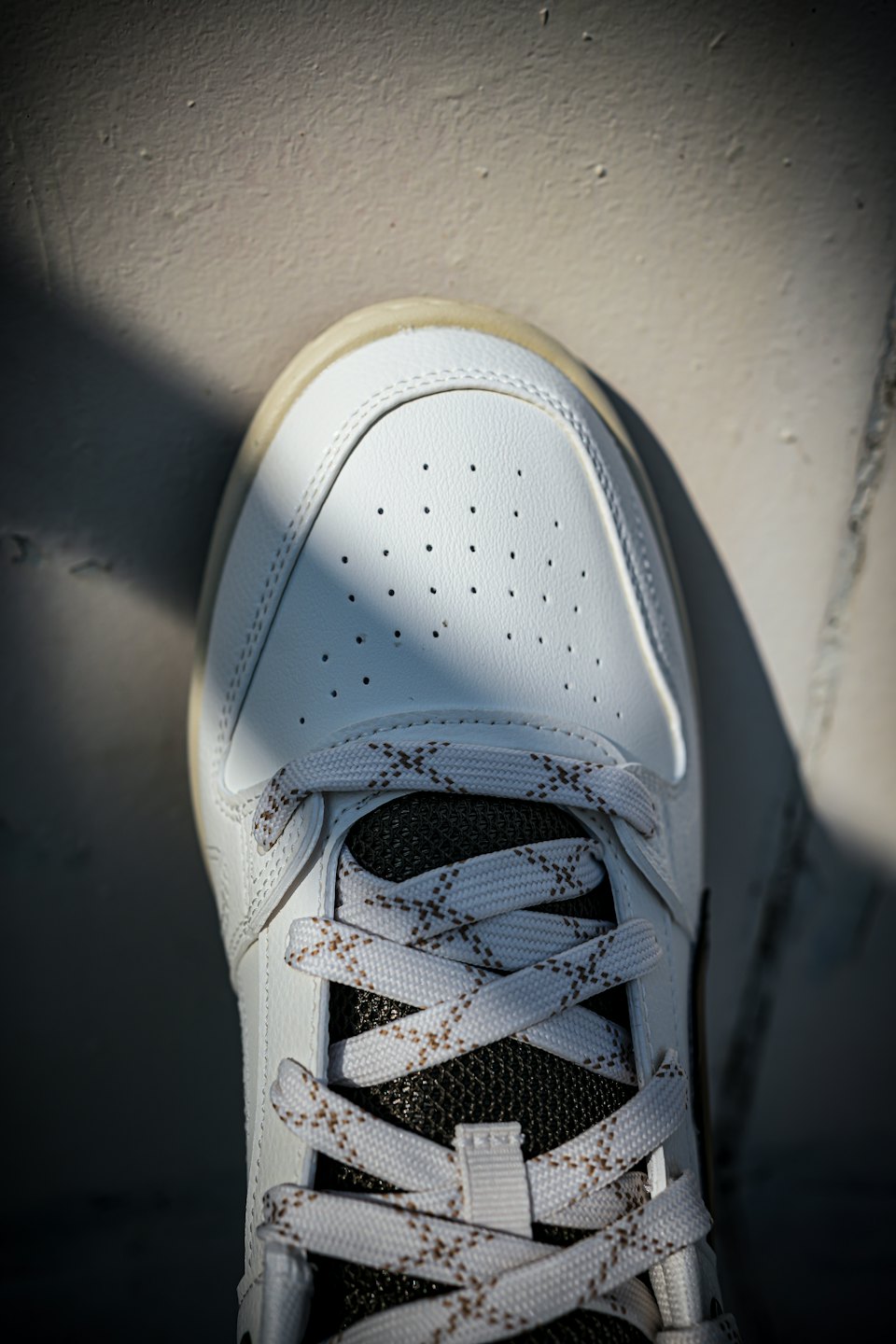 Ein weißer Leder-Sneaker mit braunen Schnürsenkeln liegt auf Beton.