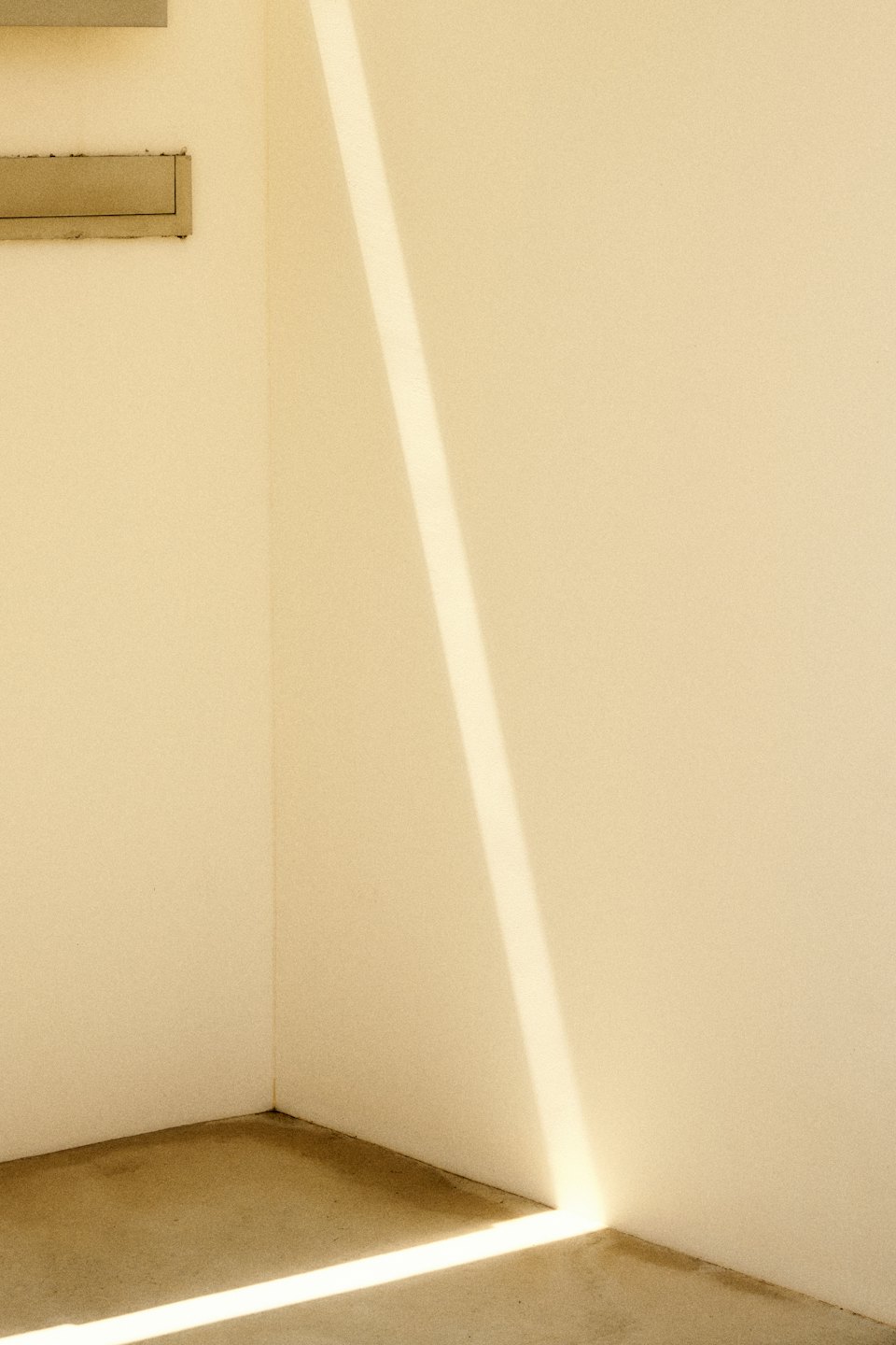 Sonnenlicht beleuchtet die Ecke von zwei beigen Wänden und einem Betonboden.
